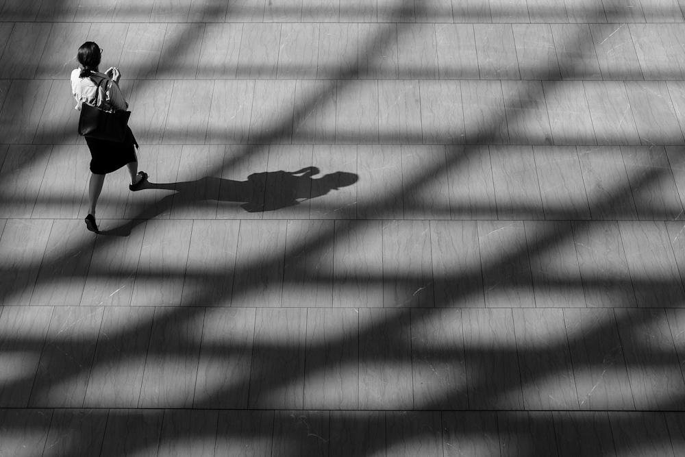 A woman walks across a tiled floor patterned with strong geometric shadows.