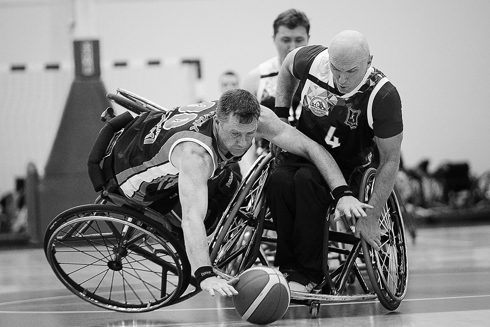 Two wheelchair basketball players reach for the ball during a match.